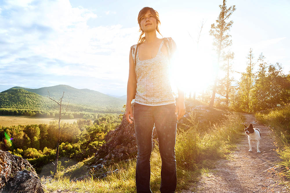 Junge Frau geht in der sonnigen Natur mit ihrem Hund spazieren